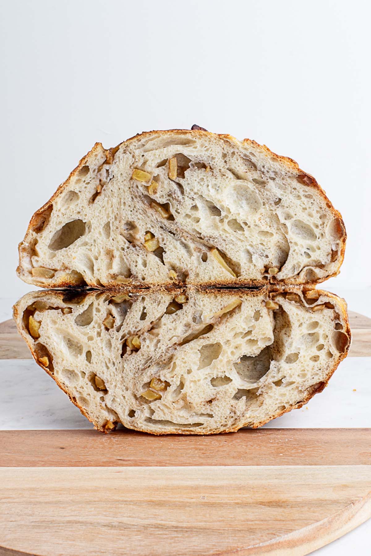 Rustic apples and cream sourdough bread cut in half on a wooden cutting board with a white background. Baked in the kitchen at Nystrom Orchard in Worthington Minnesota.
