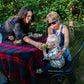 Baby eating an apple with two ladies sitting at a table in an apple orchard. Event hosted by Nystrom Orchard in Worthington Minnesota.