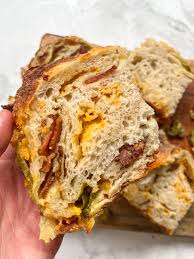Hand holding a slice of rustic bacon and cheddar sourdough bread with a white background. Baked in the kitchen at Nystrom Orchard in Worthington Minnesota.