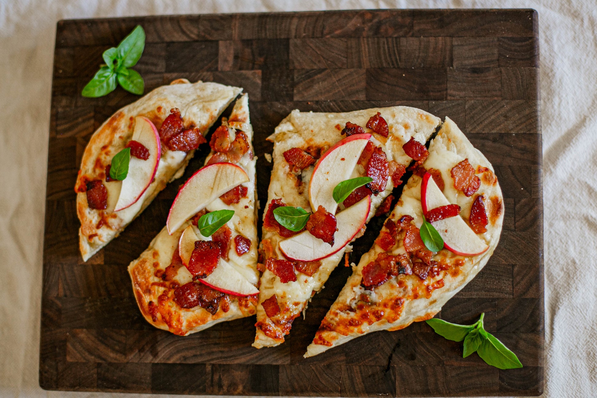 Sliced flatbread pizza with bacon cheddar and apple and basil on a dark cutting board on a white surface. Baked in the kitchen of Nystrom Orchard in Worthington Minnesota.