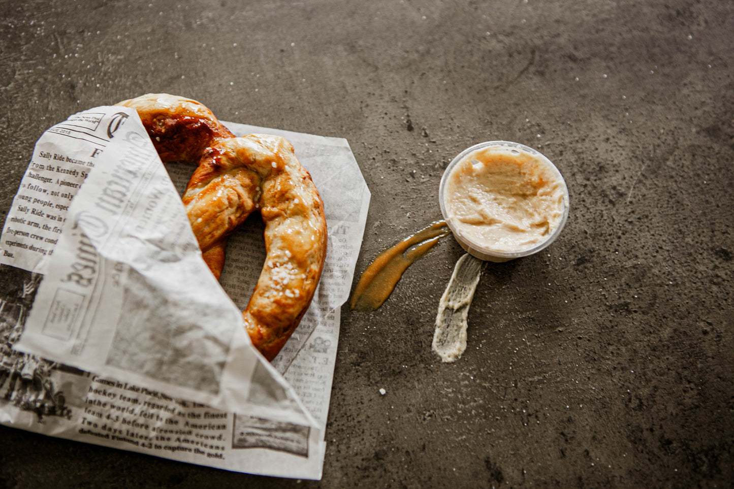 Baked Soft Pretzel in newspaper wrapping with apple pie dip on a dark surface. Made in the kitchen of Nystrom Orchard in Worthington Minnesota.