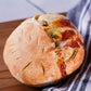 Artisan loaf of sourdough bread swirled with mozzarella cheese and fresh basil on a wooden cutting board with a black and white striped towel. Baked in the kitchen at Nystrom Orchard in Worthington Minnesota.