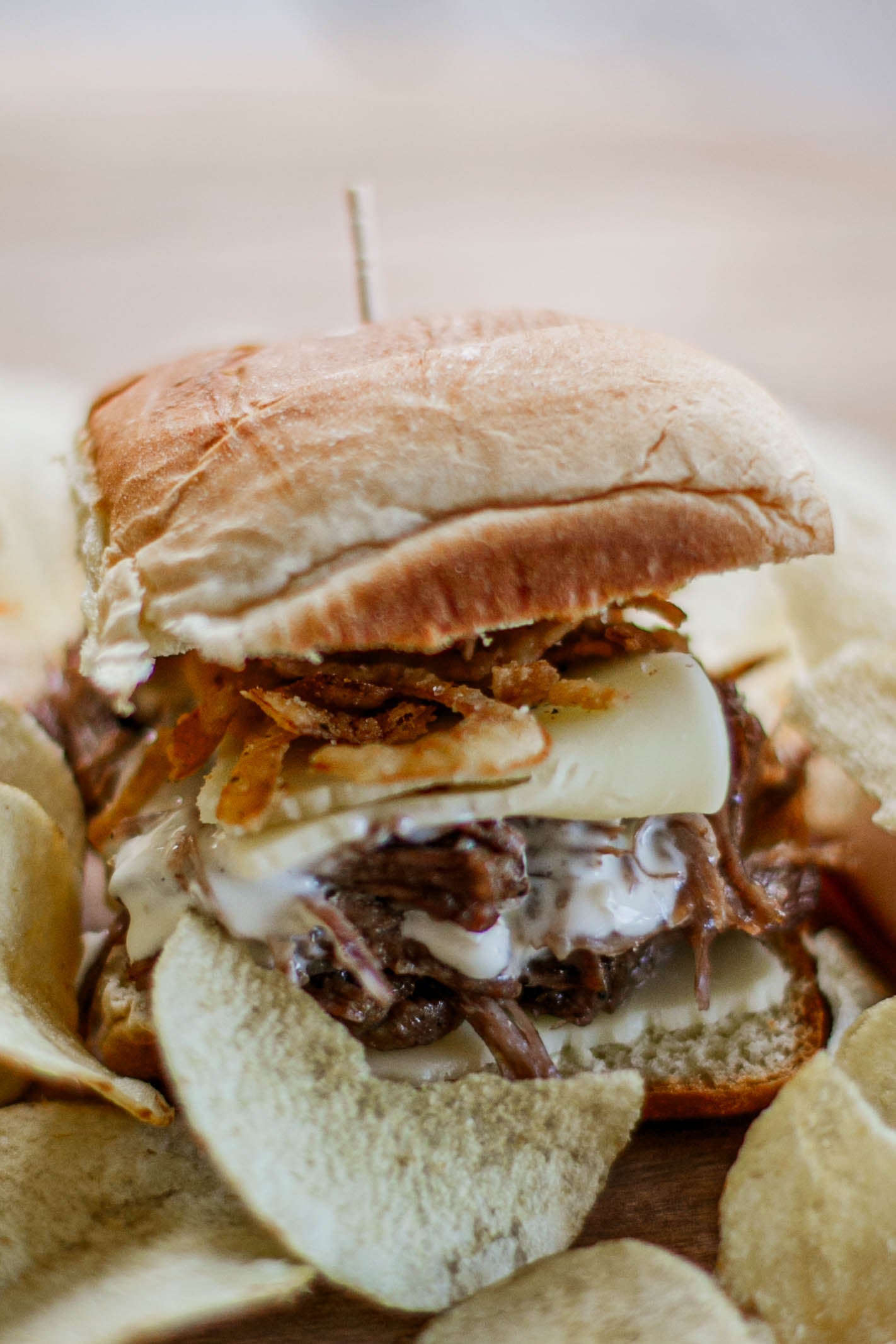 Close up of a slider packed with pulled beef, horseradish sauce, provolone and crispy onions, surrounded by chips. Made in the kitchen of Nystrom Orchard in Worthington Minnesota.