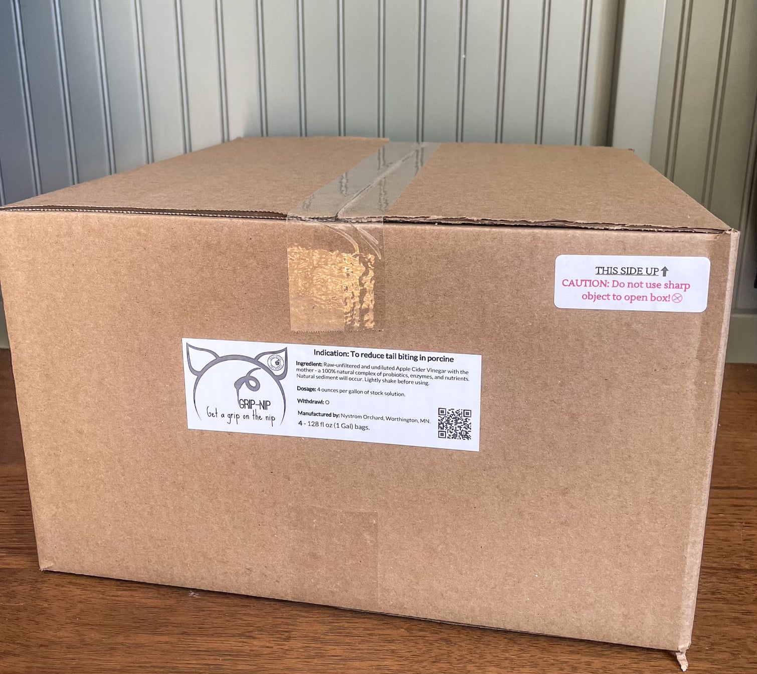 Box of Nip and Grip that is taped shut on a wooden table with a wood panels background. Made in the kitchen of Nystrom Orchard in Worthington Minnesota.