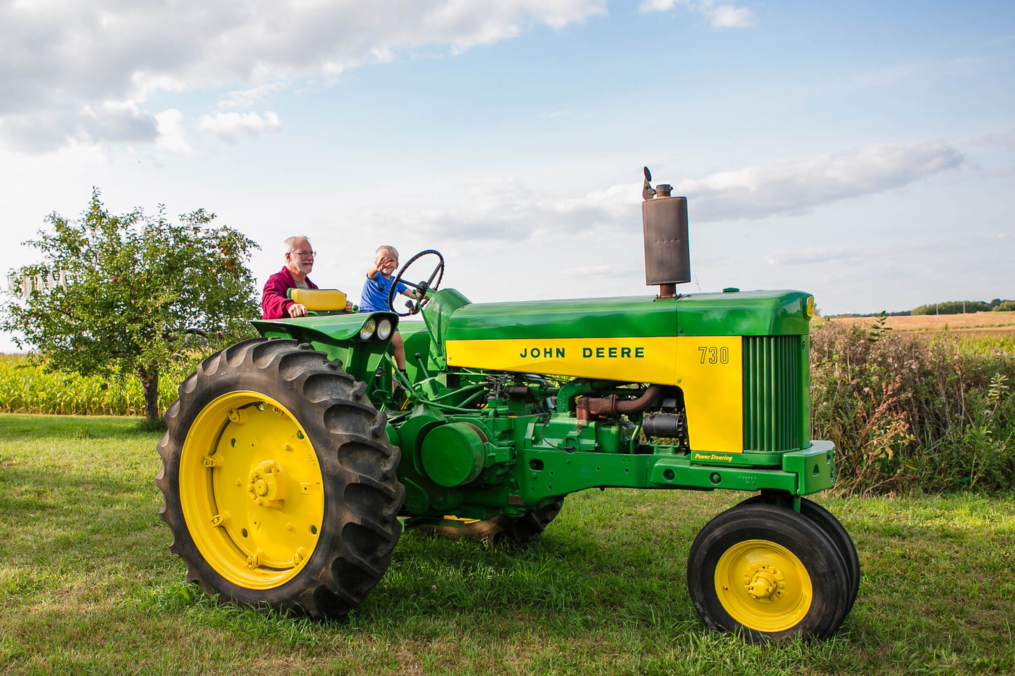 Boy and his grandpa on an old tractor beside a field with an apple tree in the background. Event hosted by Nystrom Orchard in Worthington Minnesota.
