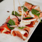 White tray of brie and apples wrapped in prosciutto with a basil leaf and drizzled with balsamic vinegar. Made in the kitchen of Nystrom Orchard in Worthington Minnesota.