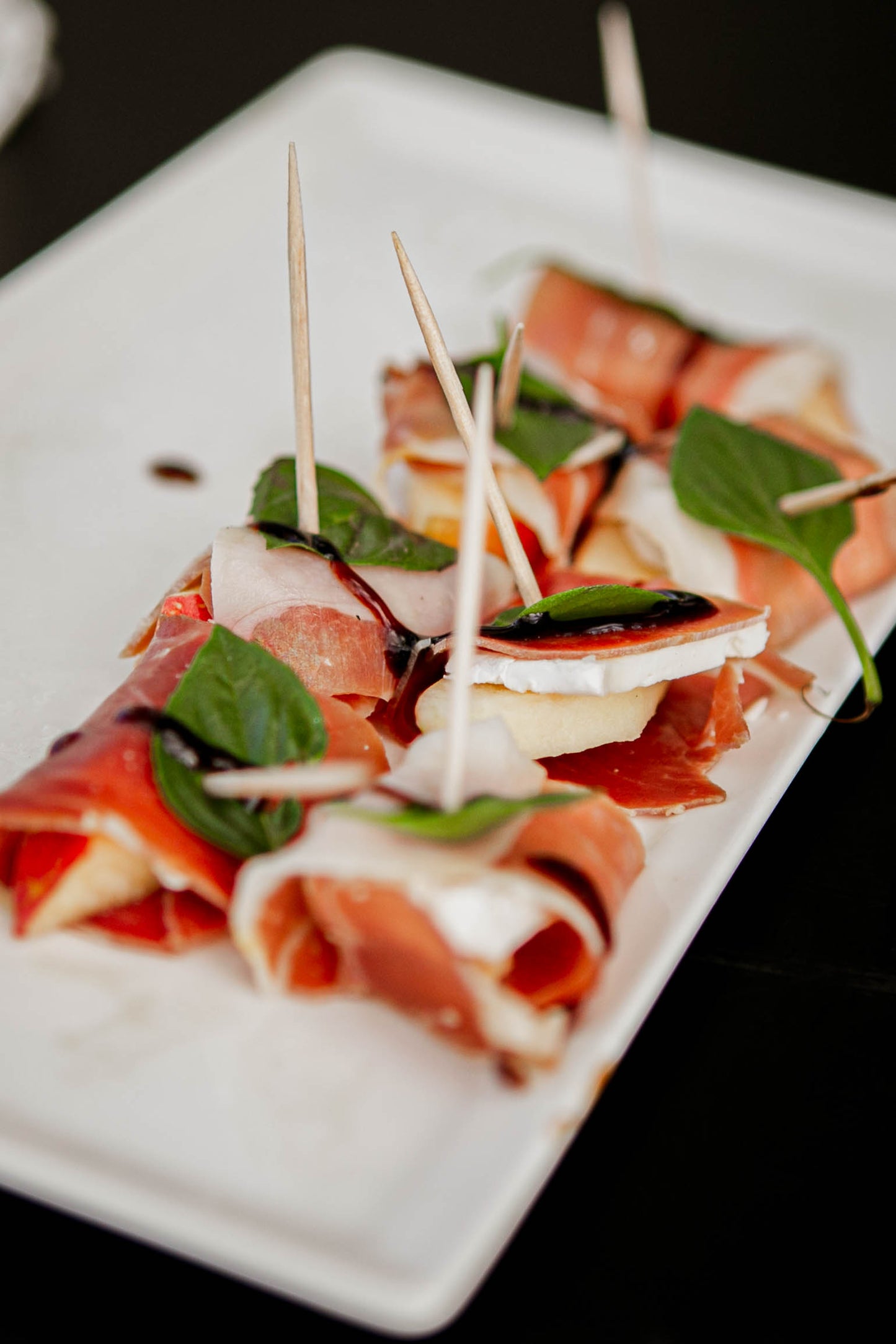 White tray of brie and apples wrapped in prosciutto with a basil leaf and drizzled with balsamic vinegar. Made in the kitchen of Nystrom Orchard in Worthington Minnesota.