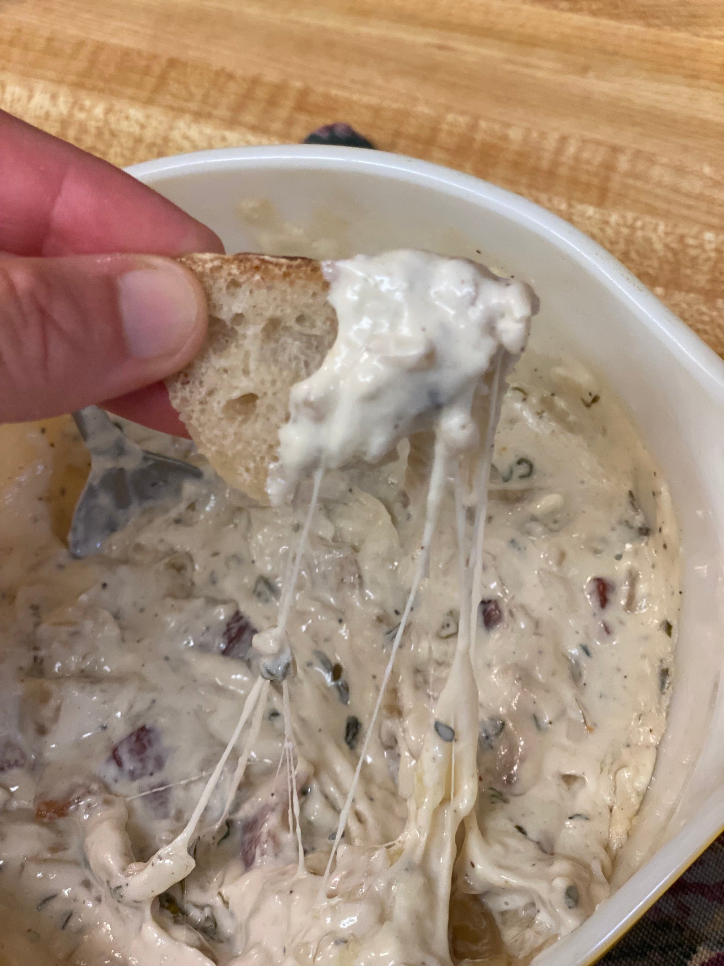 Caramelized onion cream cheese dip with a piece of bread being dipped into it on a wooden surface.