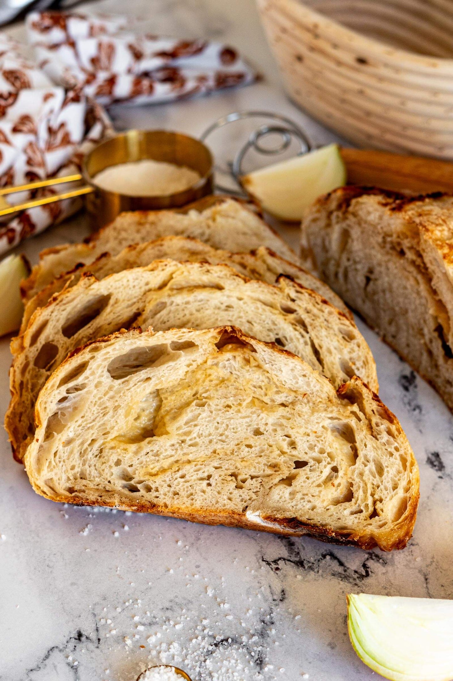 Artisan loaf of sourdough bread filled with onions and gouda sliced on a marble surface with onions and a measuring cup in the background. Baked in the kitchen at Nystrom Orchard in Worthington Minnesota. 