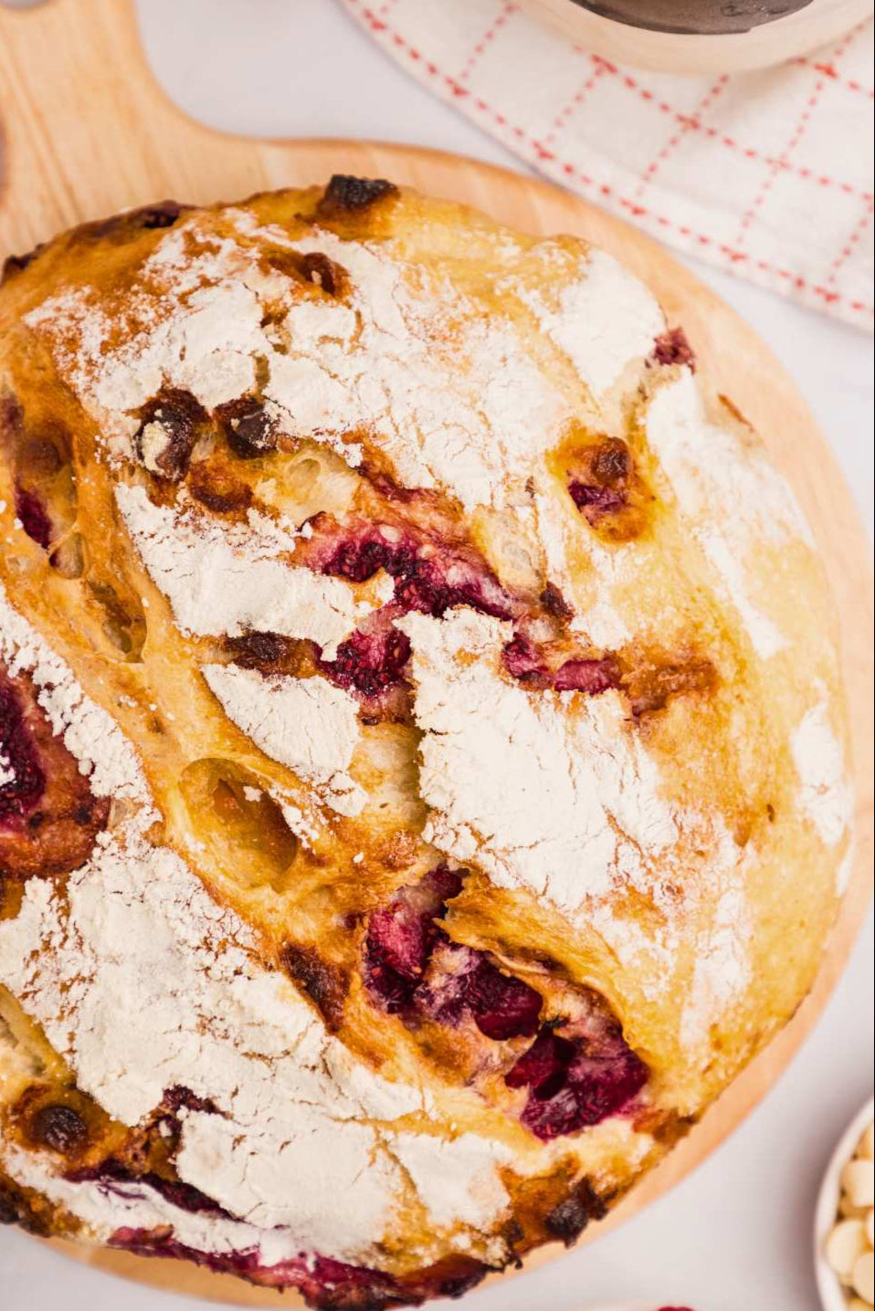 Artisan loaf of cherry and white chocolate sourdough bread on a wooden cutting board with a white surface. Baked in the kitchen on Nystrom Orchard in Worthington Minnesota.