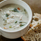 White mug of chicken and rice soup with bread on the side on a dark surface. Made in the kitchen of Nystrom Orchard in Worthington Minnesota.