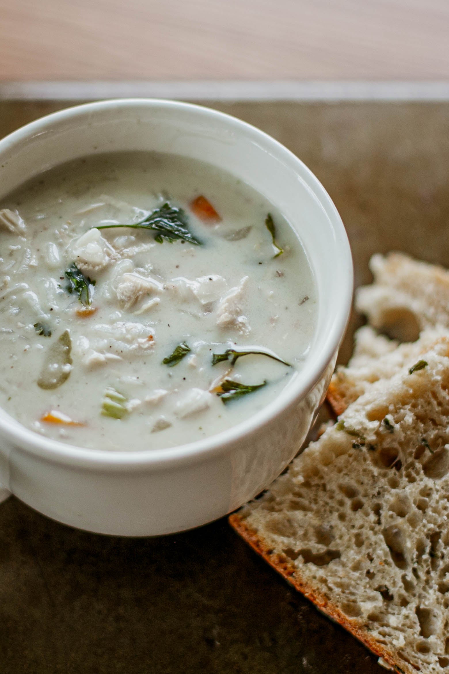 White mug of chicken and rice soup with bread on the side on a dark surface. Made in the kitchen of Nystrom Orchard in Worthington Minnesota.