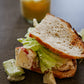 A chicken salad sandwich with lettuce on sourdough bread with a honey mustard dipping sauce on a dark surface. Made in the kitchen of Nystrom Orchard in Worthington Minnesota.