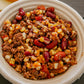 A bowl of hearty chili with visible ground beef, beans, corn and tomatoes on a wooden surface. Made in the kitchen of Nystrom Orchard in Worthington Minnesota.
