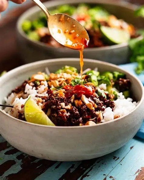 A bowl of fluffy rice topped with seasoned ground beef and fresh crunchy vegetables. We top it with an optional house made chili oil and creamy ranch. Made by Nystrom Orchard in Worthington Minnesota.