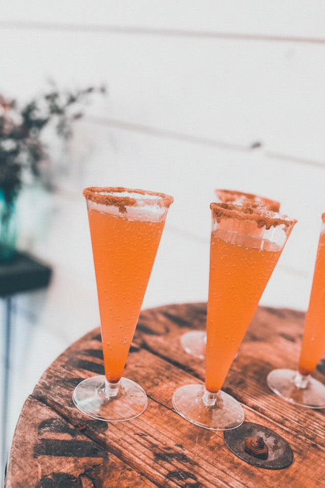 Several flutes with cinnaman sugar on the rims and a cider mocktail in the glass on a wooden surface with some greenery decorations in the background. Made in the kitchen of Nystrom Orchard in Worthington Minnesota.