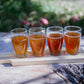 Cold pressed cider flight outside on a live edged table with blurry nature in the background. Pressed kitchen at Nystrom Orchard in Worthington Minnesota.
