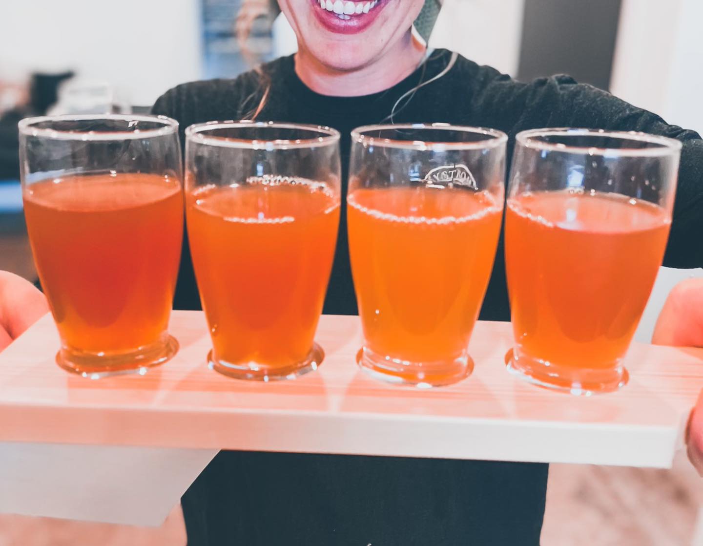 Person holding a wooden board with cold pressed cider flight. Pressed at Nystrom Orchard in Worthington Minnesota.