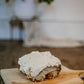 Single sourdough cinnamon roll with cream cheese frosting on a cutting board with a blurry background. Baked in the kitchen of Nystrom Orchard in Worthington Minnesota.