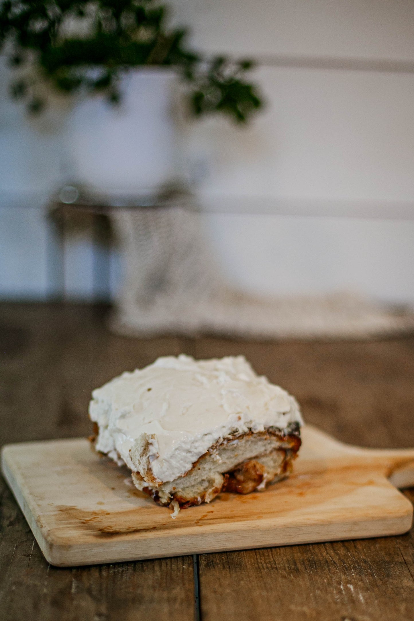 Single sourdough cinnamon roll with cream cheese frosting on a cutting board with a blurry background. Baked in the kitchen of Nystrom Orchard in Worthington Minnesota.