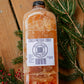 Bottle of Nystrom Orchard cold pressed cider on a wooden surface with greenery. Pressed in the kitchen of Nystrom Orchard in Worthington Minnesota.