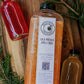 Bottle of cold pressed apple cider with a label on a wooden surface with two cider syrup bottles and greenery. Created in the kitchen of Nystrom Orchard in Worthington Minnesota. 