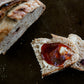 Loaf of Cranberry cream cheese sourdough bread cut with two slices in the center of the board. The one slice is spread with butter and jam on a dark surface. Baked in the kitchen at Nystrom Orchard in Worthington Minnesota.