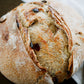 Loaf of bread with a rustic crust and visible cranberries and cream cheese on a dark surface and white cloth. Baked by Nystrom Orchard in Worthington Minnesota.