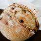 Rustic loaf of cranberry cream cheese sourdough bread on a dark surface with a white cloth. Baked in the kitchen at Nystrom Orchard in Worthington Minnesota.