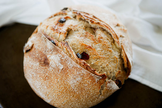 Rustic loaf of cranberry cream cheese sourdough bread on a dark surface with a white cloth. Baked in the kitchen at Nystrom Orchard in Worthington Minnesota.