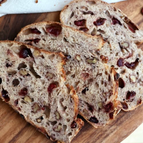 Slices of rustic cranberry walnut sourdough bread on a wooden cutting board. Baked by Nystrom Orchard in Worthington Minnesota. 