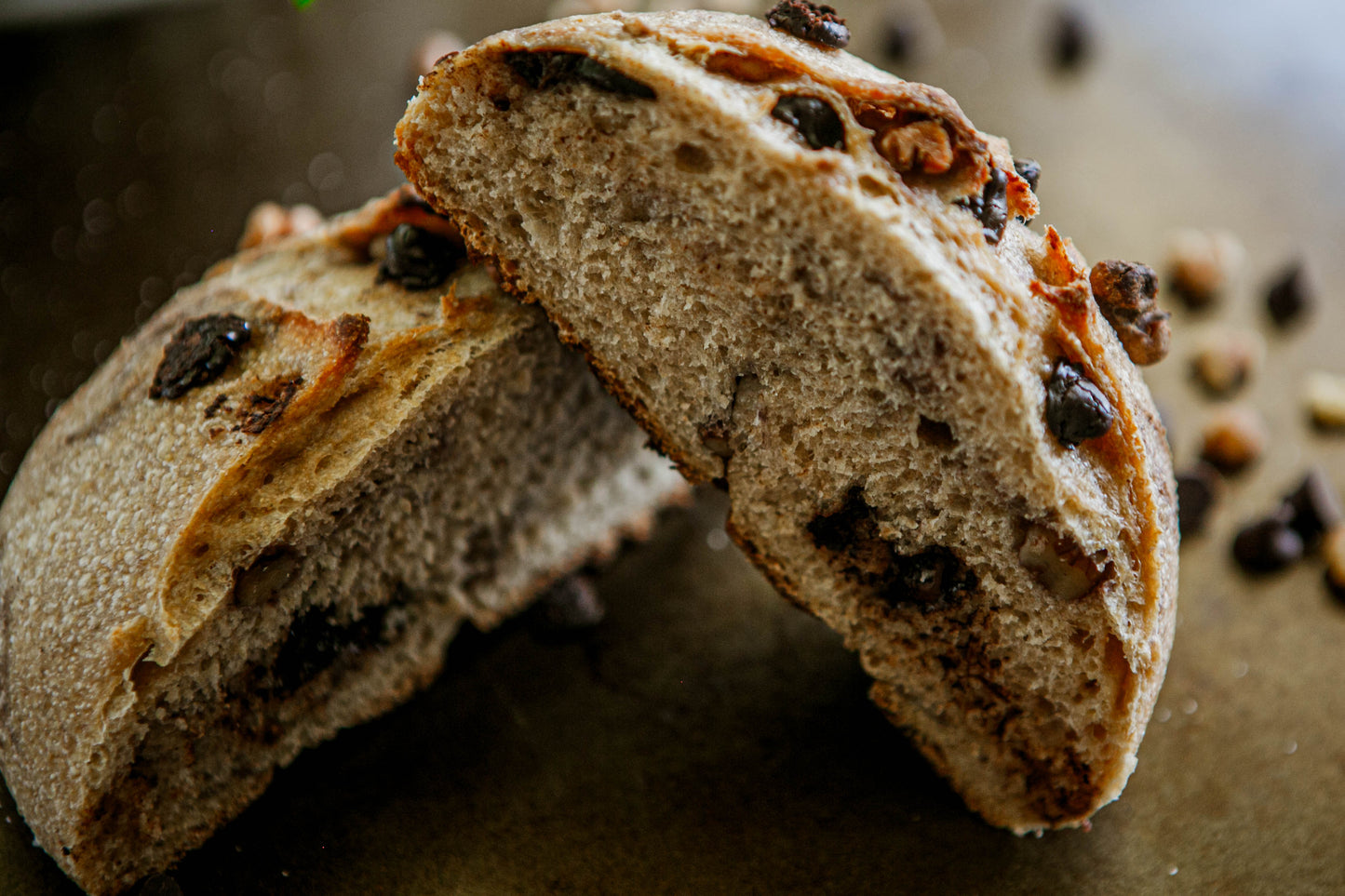 Rustic loaf of Dark Chocolate walnut sourdough on a dark surface cut in half and propped on each other. Baked in the kitchen at Nystrom Orchard in Worthington Minnesota.