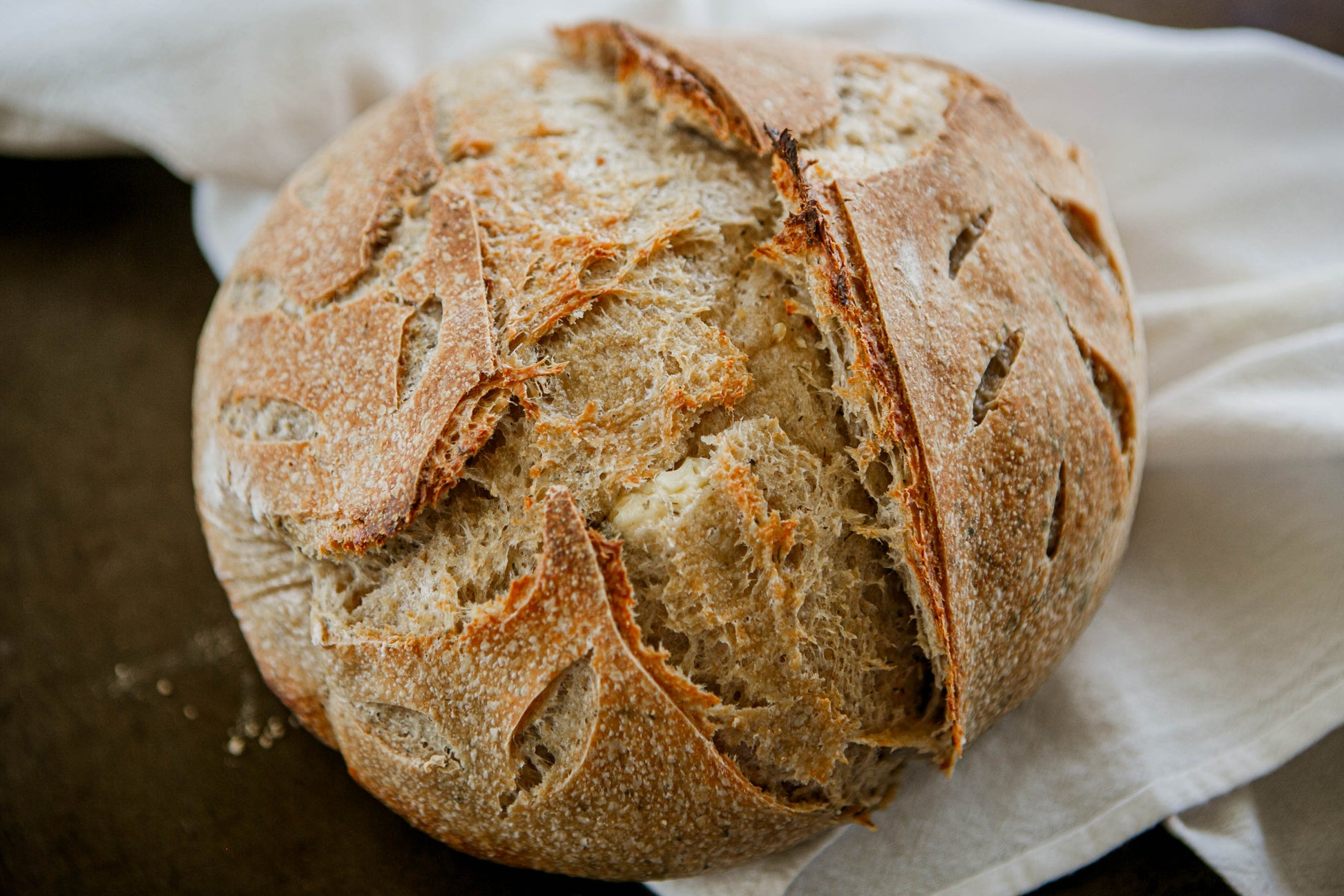 Loaf of rustic artisan dill garlic sourdough bread on a white cloth on a dark surface. Baked in the kitchen at Nystrom Orchard in Worthington Minnesota.