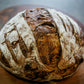 Rustic loaf of sourdough double chocolate bread on a wooden cutting board on a dark surface. Baked in the kitchen of Nystrom Orchard in Worthington Minnesota. 