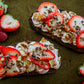 Two slices of bread topped with whipped cream, strawberries, shaved chocolate and nuts on a dark surface with fresh strawberries beside. Prepared in the kitchen at Nystrom Orchard in Worthington Minnesota. 