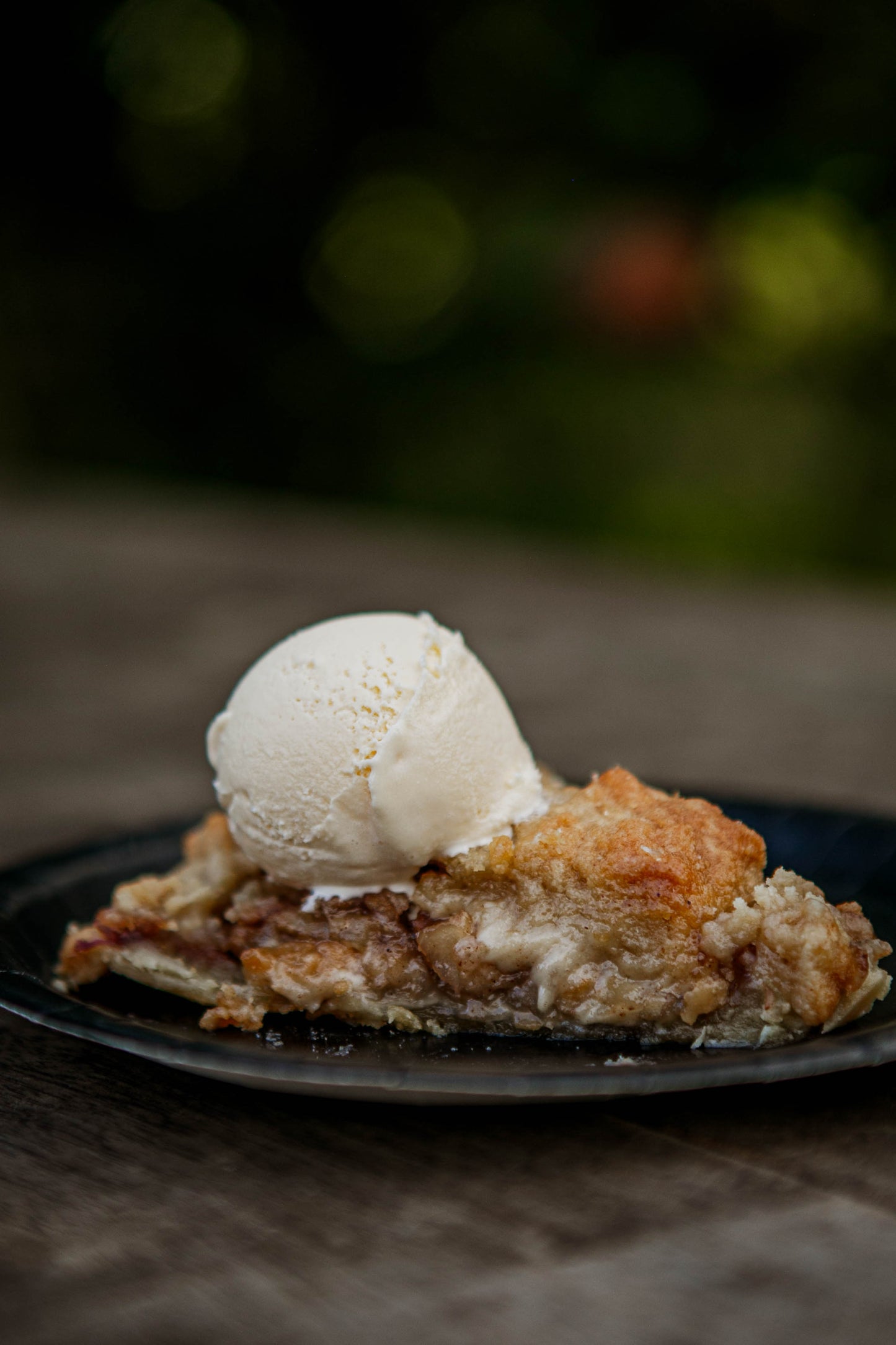 Slice of dutch apple pie with a scoop of ice cream on a dark plate against a blurred background. Baked in the kitchen of Nystrom Orchard in Worthington Minnesota.