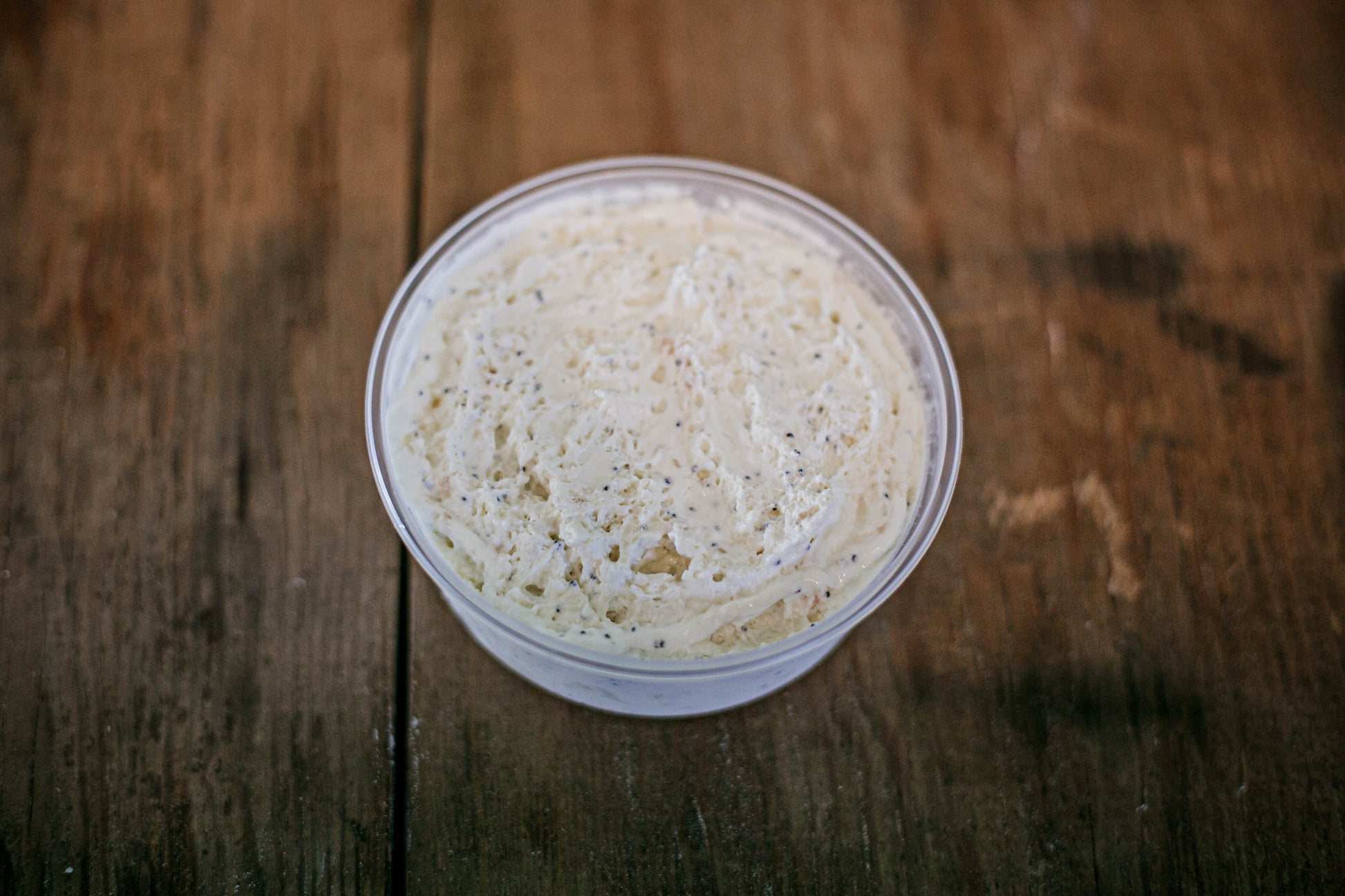 Plastic container filled with everything bagel dip on a wooden surface.  Made in the kitchen of Nystrom Orchard in Worthington Minnesota.