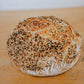 A freshly baked loaf of artisan everything bagel sourdough bread on a wooden cutting board. Baked in the kitchen of Nystrom Orchard in Worthington Minnesota.