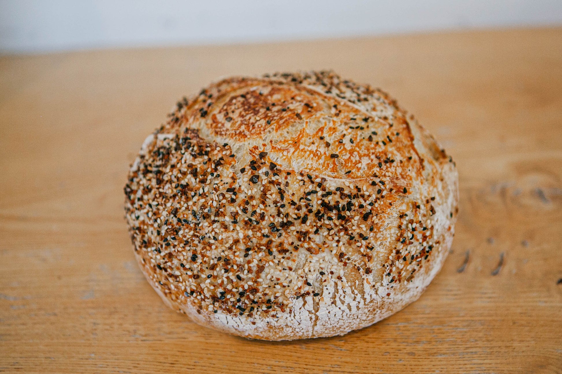 A freshly baked loaf of artisan everything bagel sourdough bread on a wooden cutting board. Baked in the kitchen of Nystrom Orchard in Worthington Minnesota.