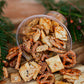 Sourdough snack mix in a clear container on a wooden surface with greenery in the background. Made in the kitchen of Nystrom Orchard in Worthington Minnesota.