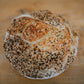 Loaf of rustic sourdough bread covered in everything bagel seasoning on a wooden surface. Baked by Nystrom Orchard in Worthington Minnesota.