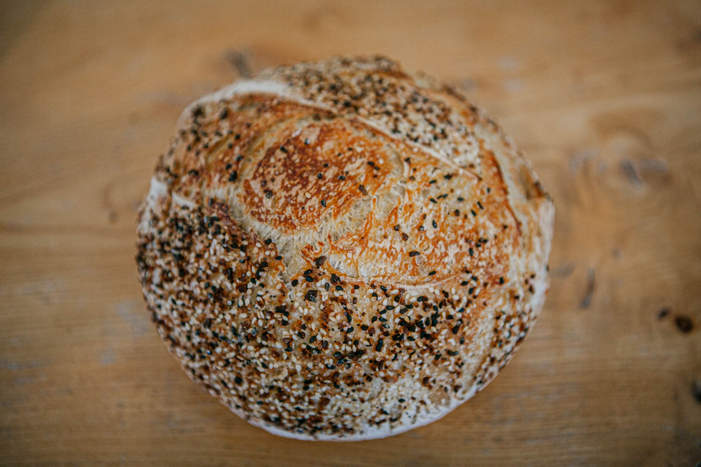 Loaf of rustic sourdough bread covered in everything bagel seasoning on a wooden surface. Baked by Nystrom Orchard in Worthington Minnesota.