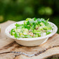 A fall salad with red onion, walnuts, and parmesan in a white paper bowl on a wooden table with an apple behind. Made in the kitchen of Nystrom Orchard in Worthington Minnesota. 