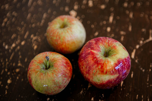 Three apples that are the variety frostbite on a brown wooden table. Apples from the orchard of Nystrom Orchard in Worthington Minnesota.