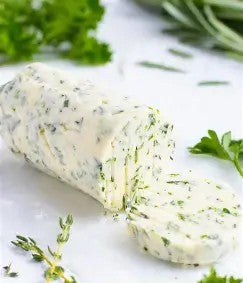 Rolled herbed compound butter on a white background with fresh herbs around. Created in the kitchen of Nystrom Orchard in Worthington Minnesota.