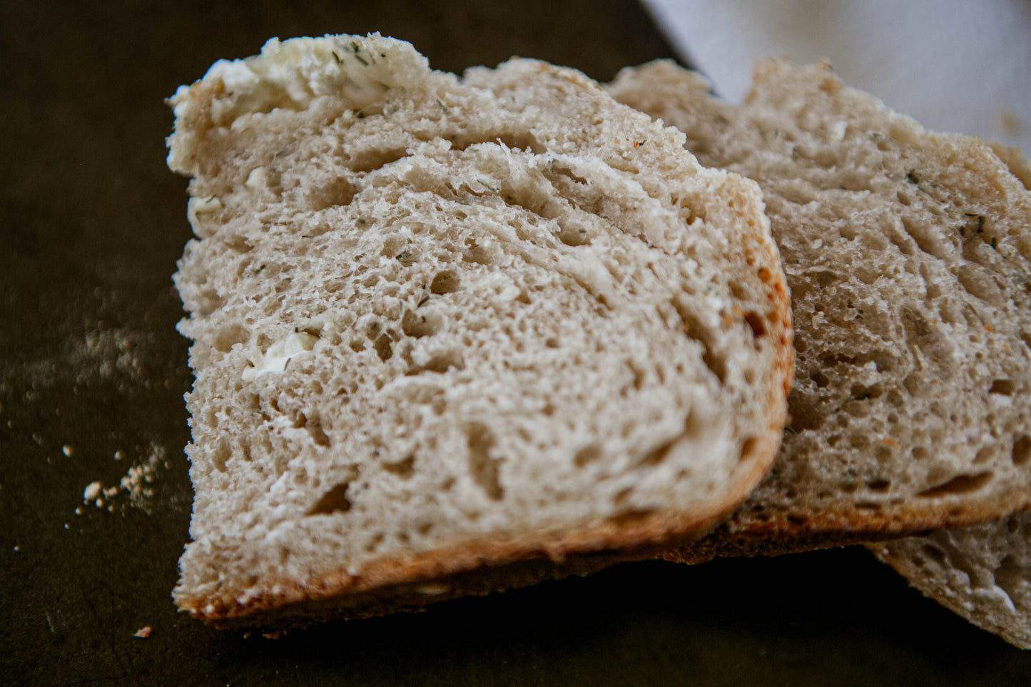 Two slices of herbed rustic sourdough bread on a dark surface. Baked in the kitchen of Nystrom Orchard in Worthington Minnesota.