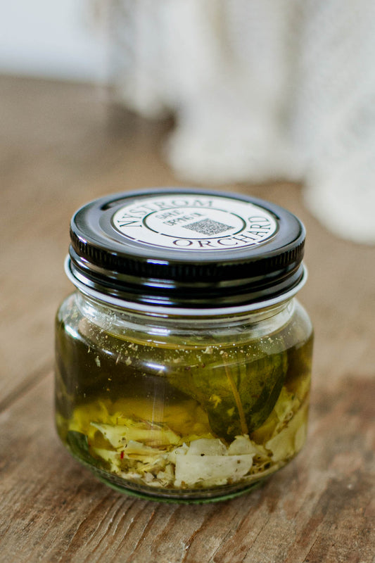 Glass jar of garlic dipping olive oil with parmesan cheese and fresh basil and a black lid on a wooden surface. Made in the kitchen at Nystrom Orchard in Worthington Minnesota. 