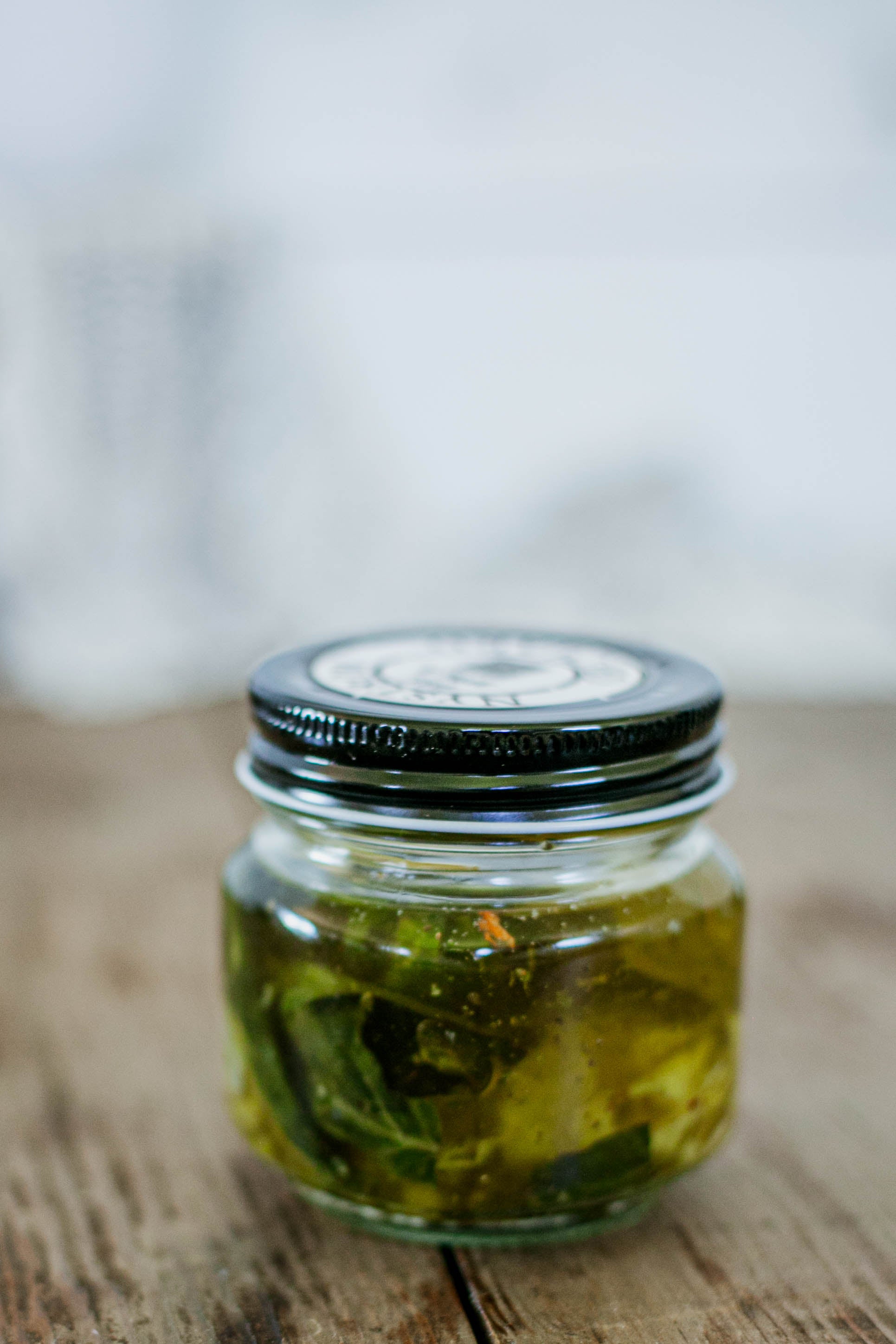 Glass jar of garlic dipping olive oil with parmesan cheese and fresh basil and a black lid on a wooden surface. Made in the kitchen at Nystrom Orchard in Worthington 