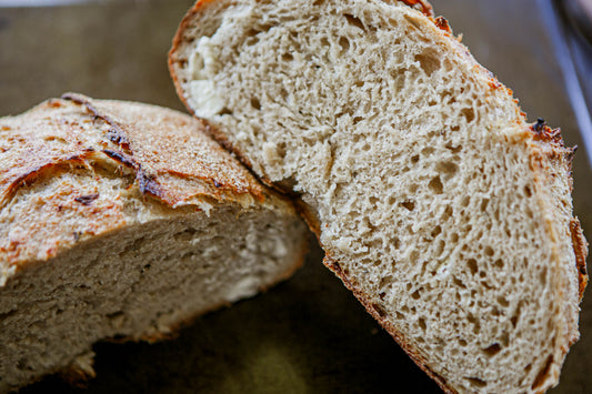 Close up of a rustic loaf of garlic rosemary sourdough bread cut in half so you can see the crumb on the inside on a dark surface. Baked in the kitchen at Nystrom Orchard in Worthington Minnesota.