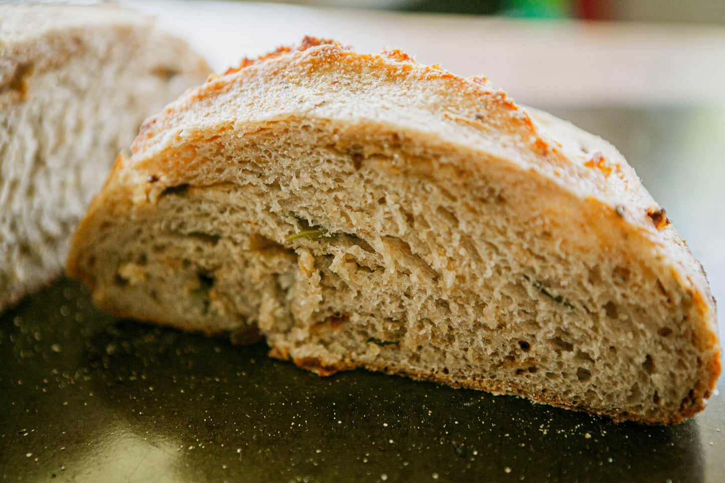 Loaf of garlic and herb sourdough cut in half so you can see the crumb on a dark surface. Baked in the kitchen at Nystrom Orchard in Worthington Minnesota.